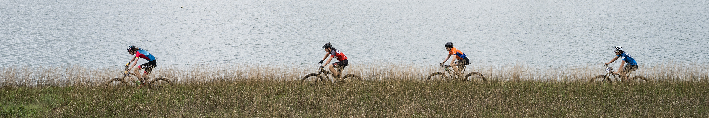 Mountain bikers ride along a lake at Xcel Energy MTB park